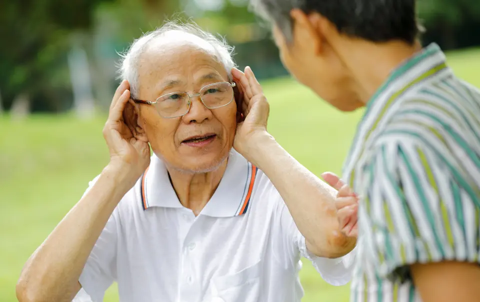Elderly man putting hands to ears to hear better