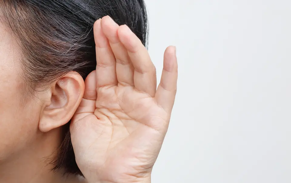 Asian woman holding hand to ear to listen