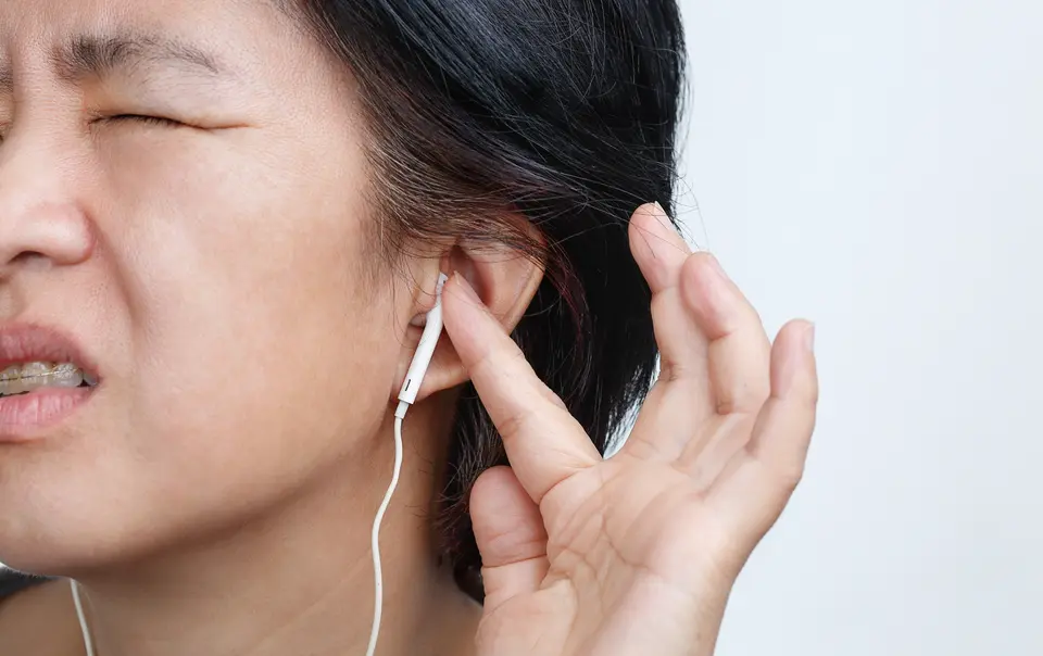 Woman who seems to be in pain from loud music on the headphones